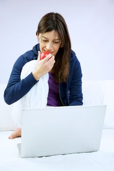 Woman smiling eats apple sitting in front of computer 