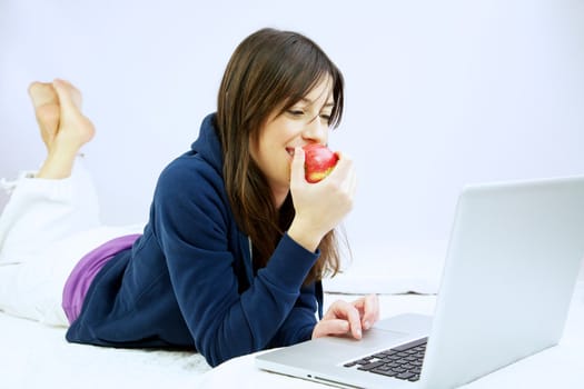 Woman smiling happy  eats apple in front of computer laying in bed