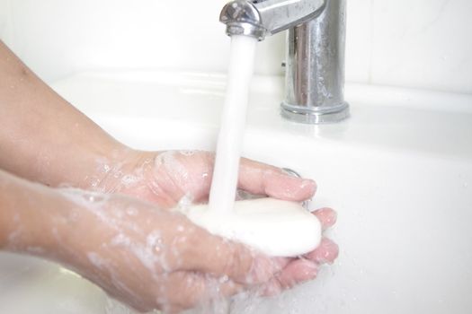 Hands being washed with soap under a tap 