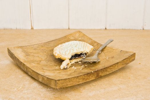 Unusual rustic image of a half-eaten mince pie on a wooden plate