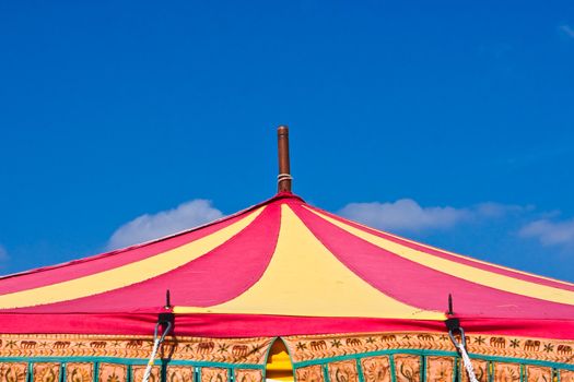 A brightly colored circus tent top against a bright blue sky