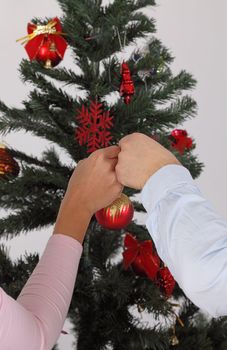 Images of a man's and a woman's hands putting together a bauble on a Christmas tree.