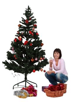 Studio shot of a young brunette decorating the Christmas tree against a white background.