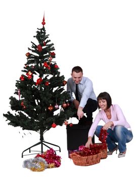 Studio shot of a young happy couple decorating the Christmas tree, against a white background.