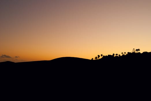 The dark silhouette of sand and trees in the south of the island at sunset