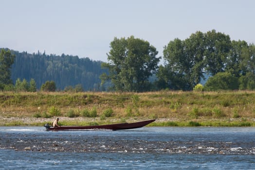 Man floats on a long wooden boat on a mountain river