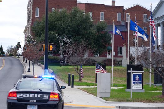 Plolice car with lights on blocking the road, with flags blowing.