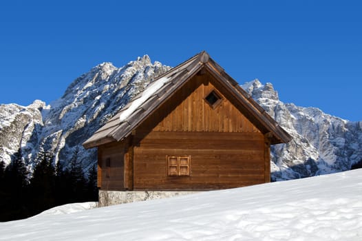 Wooden chalet in winter with snow-capped peaks - Alps Italy