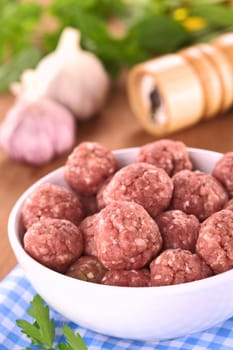 Raw meatballs with garlic in a white bowl (Selective Focus, Focus on the meatballs in the front)