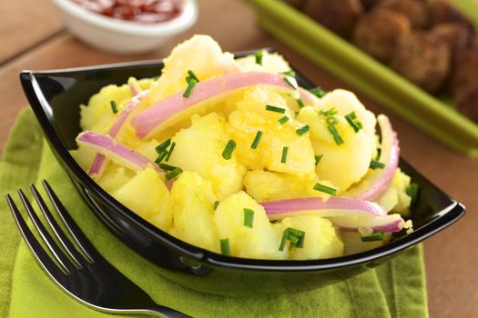 Potato salad with onions prepared in Swabian-Style (Southern Germany) with meatballs and ketchup in the back (Selective Focus, Focus one third into the bowl)