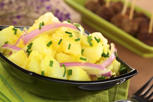 Potato salad with onions prepared in Swabian-Style (Southern Germany) garnished with chives, meatballs in the back (Selective Focus, Focus one third into the bowl)