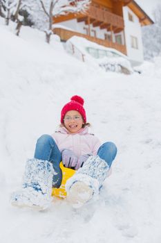 Cute pretty girl in red hat riding on a sled near the Austrian cottage
