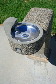 Drinking fountain on a sidewalk in a park.
