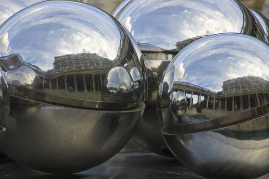Three steel spheres at Palais Royal, Paris, reflecting building and skies