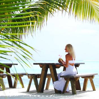 woman sitting in a tropical cafe on the background of a  palm trees and sky and sea