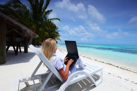 business woman with laptop lying on a chaise lounge in the tropical ocean coast