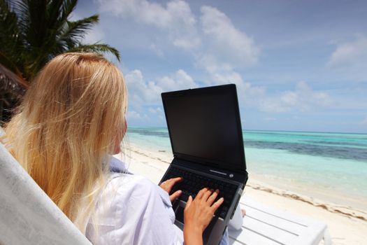 business woman with laptop lying on a chaise lounge in the tropical ocean coast