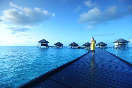 woman in a dress on a bridge home sea and the maldivian sunset on the background