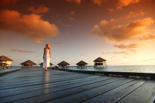 woman in a dress on a bridge home sea and the maldivian sunset on the background