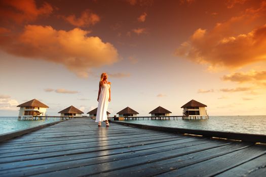 woman in a dress on a bridge home sea and the maldivian sunset on the background