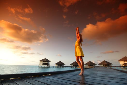 woman in a dress on a bridge home sea and the maldivian sunset on the background