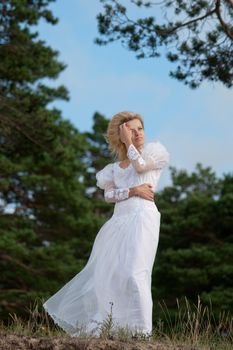 Woman standing on a cliff in a long white dress and looking into the horizon