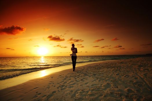 woman run along the sea coast of sunrise behind