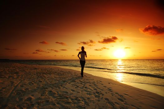 woman run along the sea coast of sunrise behind