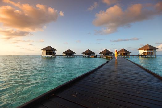 woman in a dress on a bridge home sea and the maldivian sunset on the background