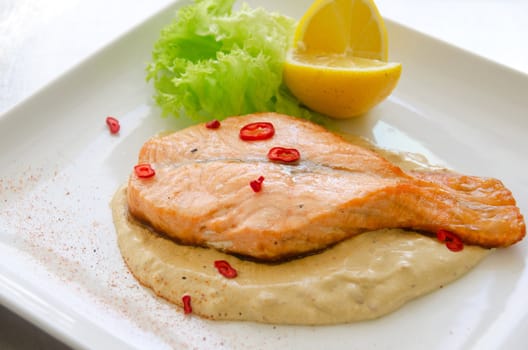 Grilled salmon steak with greens, lemon, sauce and pepper chile