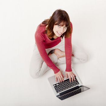 Beautiful and happy woman sitting on the floor and working with a laptop