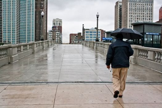 A man with an umbrella crossing a bridge