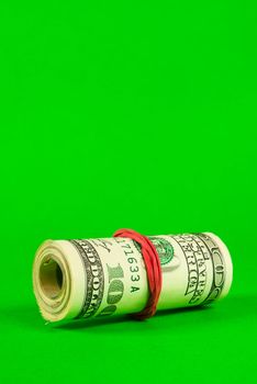 Roll of US dollars tied up with rubber over green background