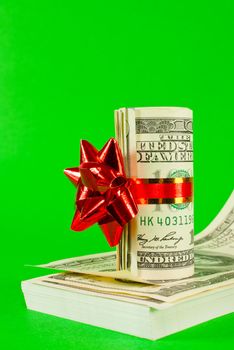 Roll of US dollars tied up with ribbon on the stack of bills over green background