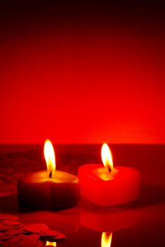 Two burning heart shaped candle on a red table