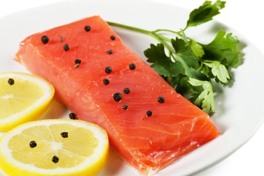 Closeup view of fresh salmon with parsley and lemon on a white plate
