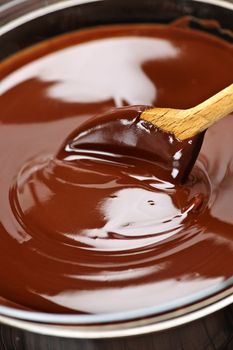 Wooden spoon stirring soft melted rich chocolate