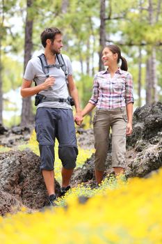 Hiking couple walking in forest. Young hikers couple enjoying romantic walk in spring forest with flowers. Happy smiling interracial couple holding hands during hike. From Tenerife, Canary Islands, Spain