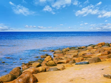 Sea rocky beach in sunny day, blue cloudy sky 