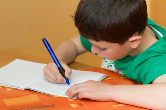 small school boy writting homework from school in workbook