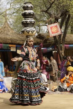 Female tribal dancer performing a dance involving balancing an increasing number of pots on her head at the annual Sarujkund Fair near Delhi, India.