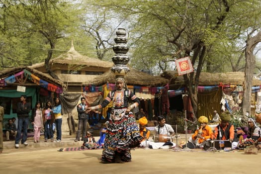 Female tribal dancer performing a dance involving balancing an increasing number of pots on her head at the annual Sarujkund Fair near Delhi, India.