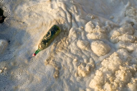 Water pollution, a bottle and foam on a river.