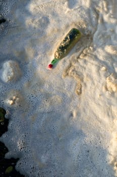 Water pollution, a bottle and foam on a river.
