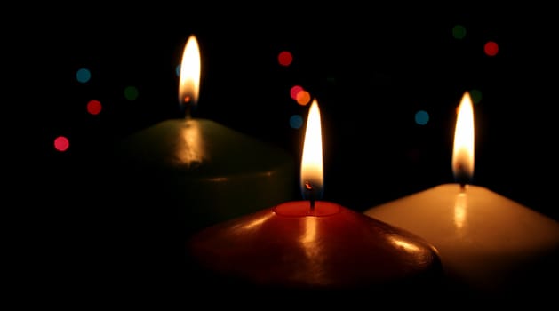 Three Christmas candles up close, with festive lights in the background.
