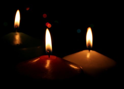 Three Christmas candles up close, with festive lights in the background.
