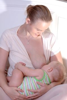 Young mother is holding and breast-feeding her little child.