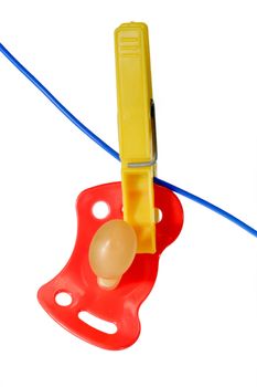 A red pacifier hangs on a cloth line. Isolated on white background
