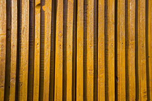 Closeup of yellow-painted wooden wall impeachment small board lit by sun.