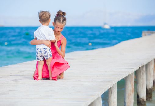 Back view of cute girl with her brother walking on jetty with turquoise sea